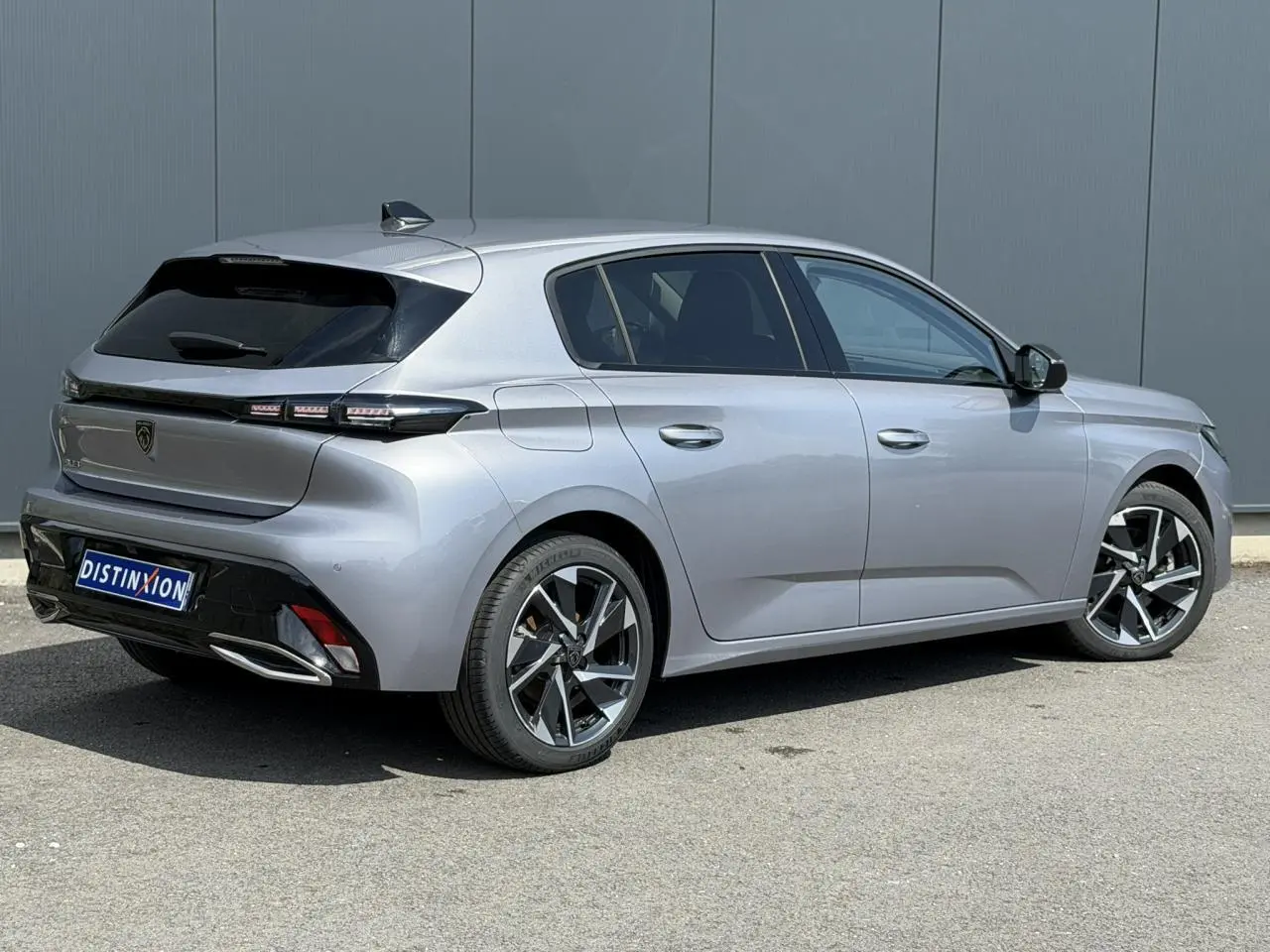 Vue 3/4 arrière droite de la Peugeot 308 2025 gris Artense avec jantes alliage 17'' et bandeau noir brillant arrière.