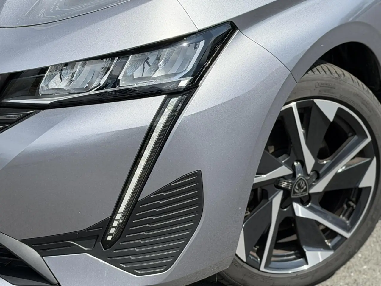 Gros plan sur l'avant droit gris Artense du Peugeot 308 2025, mettant en valeur le phare LED et la jante alliage 17 pouces.