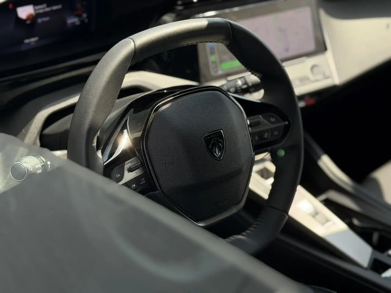 Gros plan sur le volant cuir noir de la Peugeot 308 2025, avec tableau de bord numérique et écran tactile en arrière-plan.