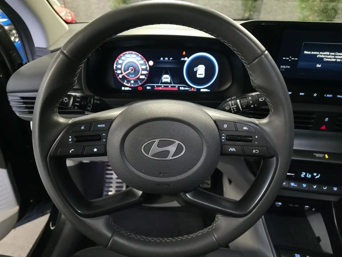 Vue intérieure centrée sur le volant cuir noir d'une Hyundai Bayon 2025 avec tableau de bord numérique et écran tactile.