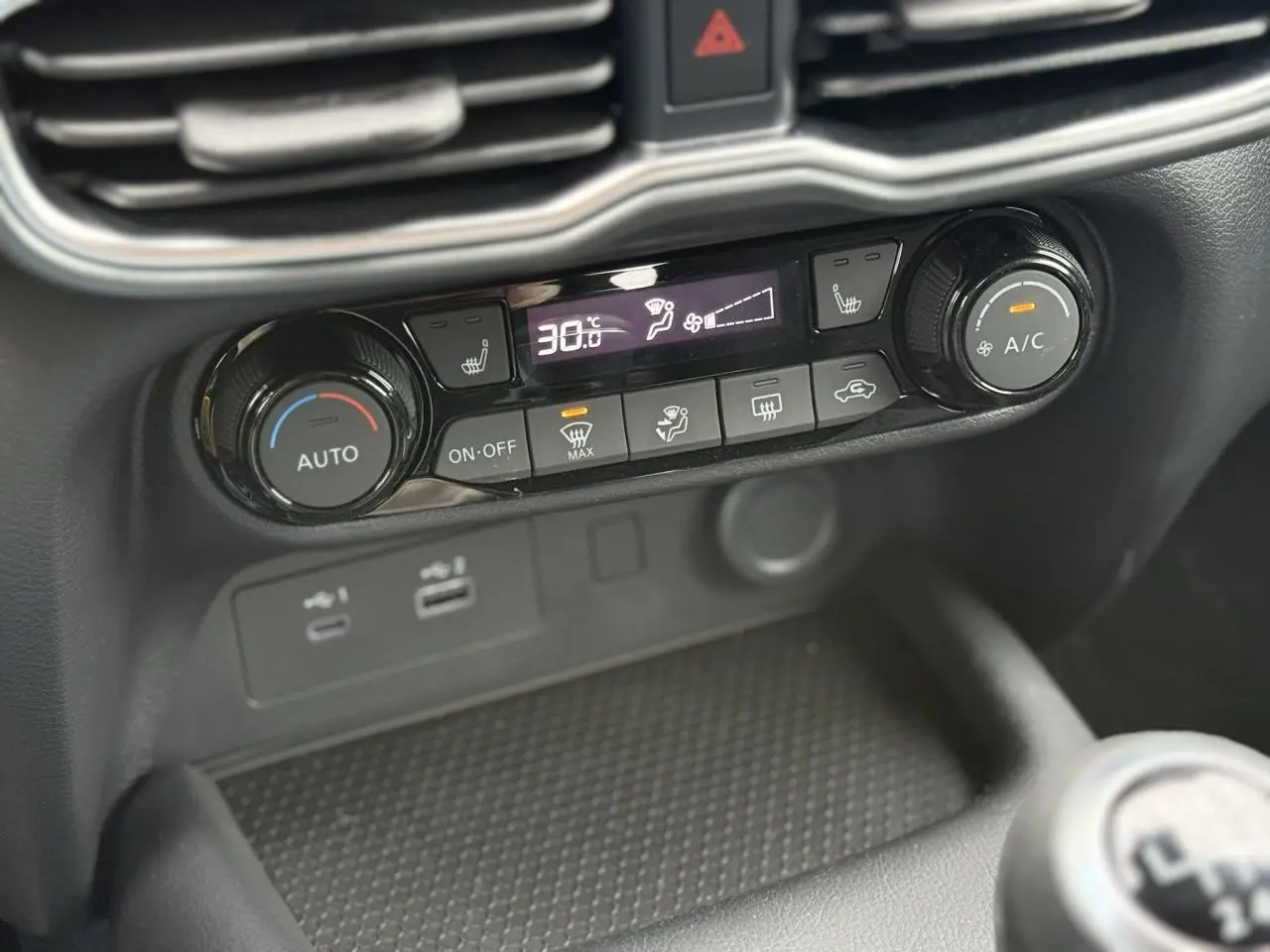 Vue rapprochée de la console centrale noire du Nissan Juke 2025, avec commandes climatisation automatique et sièges chauffants.