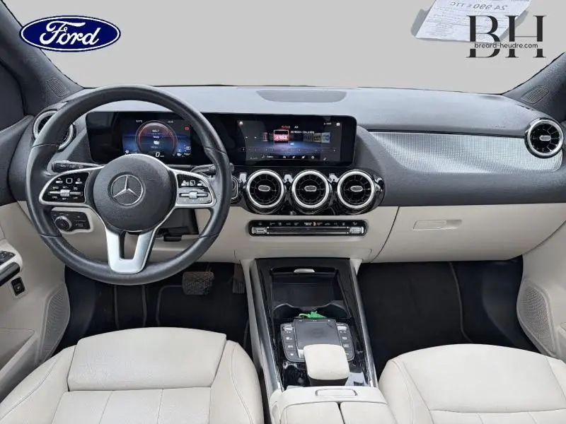 Vue intérieure avant de la Mercedes Classe B 250 e avec tableau de bord numérique et sièges en similicuir beige.