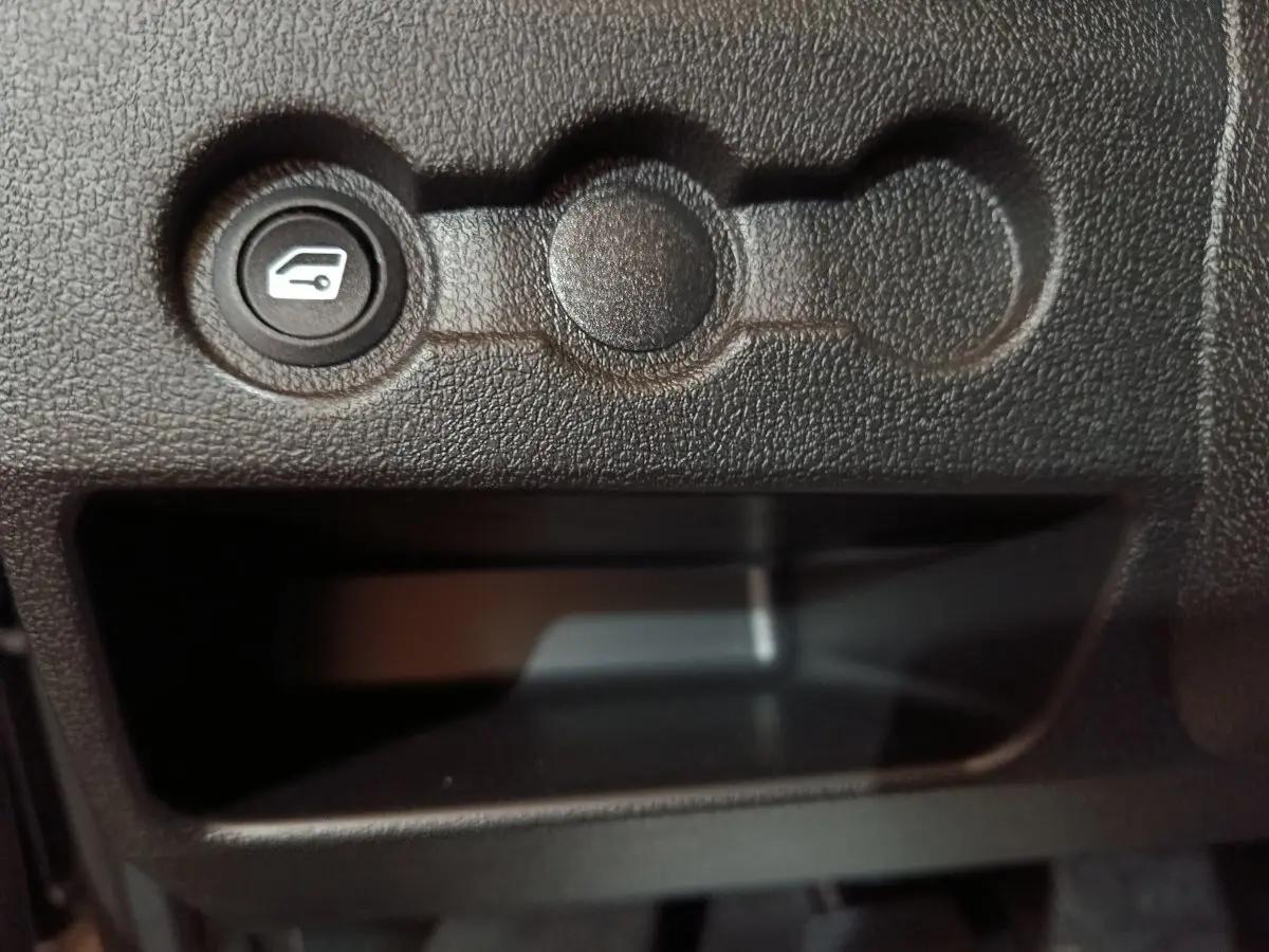 Bouton de commande de coffre sur tableau de bord noir texturé d'une Aixam Ambition 0.5 City Pack 2026.