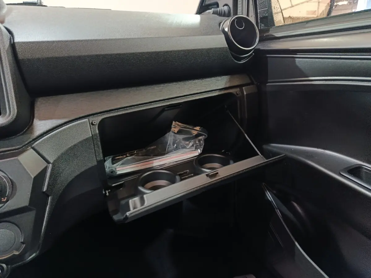 Intérieur de l'AIXAM AMBITION 0.5 CITY PACK 2026, vue sur la boîte à gants ouverte avec porte-gobelets intégrés.