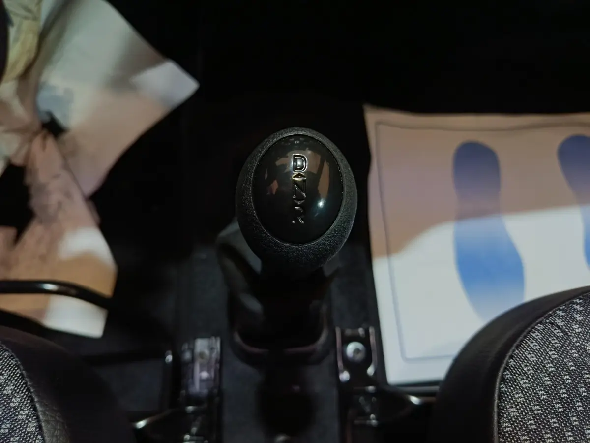 Le levier de vitesse noir marqué "DAKAR" au centre de l'habitacle d'une Aixam Ambition gris clair.