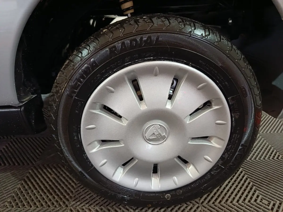 Gros plan sur la roue avant gauche d'une Aixam Ambition gris clair avec jante et logo central visibles.