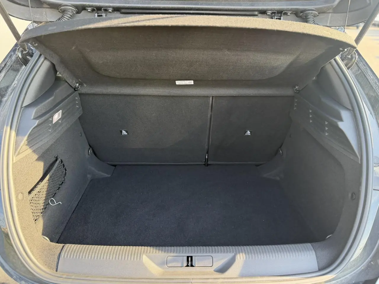 Coffre ouvert vu de l'arrière d'une Peugeot 308 noir Perla, montrant un espace de rangement vide et propre.