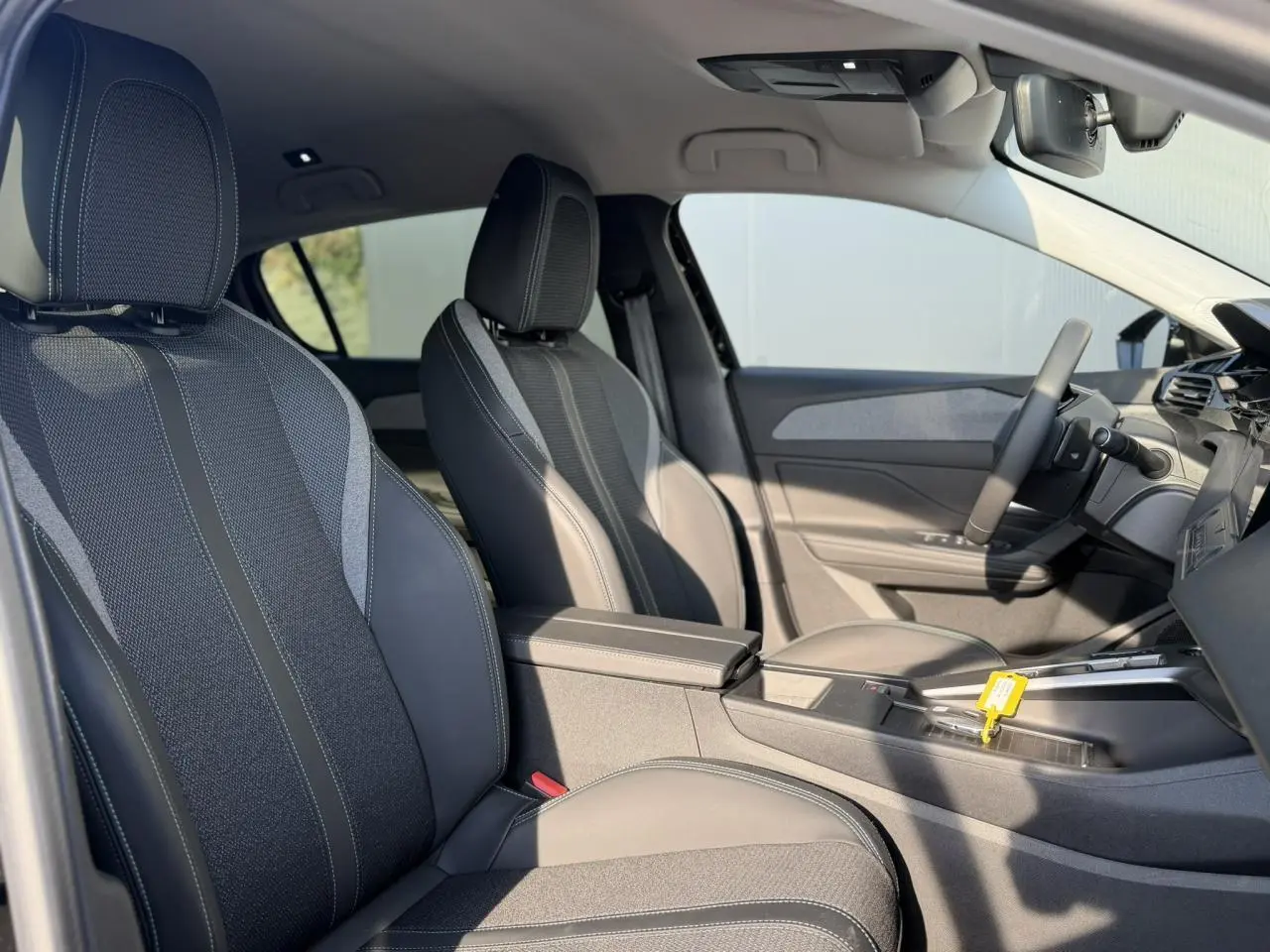 Vue intérieure côté conducteur de la Peugeot 308 2025, sièges tissu et cuir noirs avec accoudoir central.