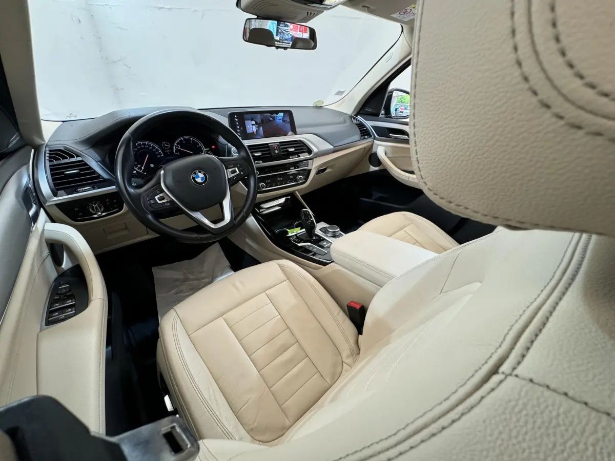 Vue intérieure côté conducteur du BMW X3 2018 avec sièges cuir beige et tableau de bord moderne avec écran tactile.