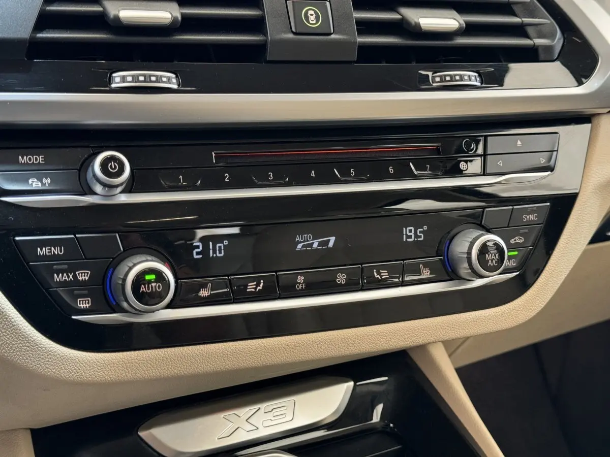 Détail du tableau de bord beige du BMW X3 xDrive30d 2018 avec commandes climatisation digitale et inscription X3.