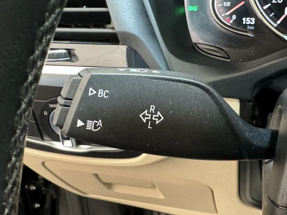 Gros plan sur la manette de clignotant noire à gauche du volant dans l'habitacle beige d'une BMW X3 gris foncé 2018.
