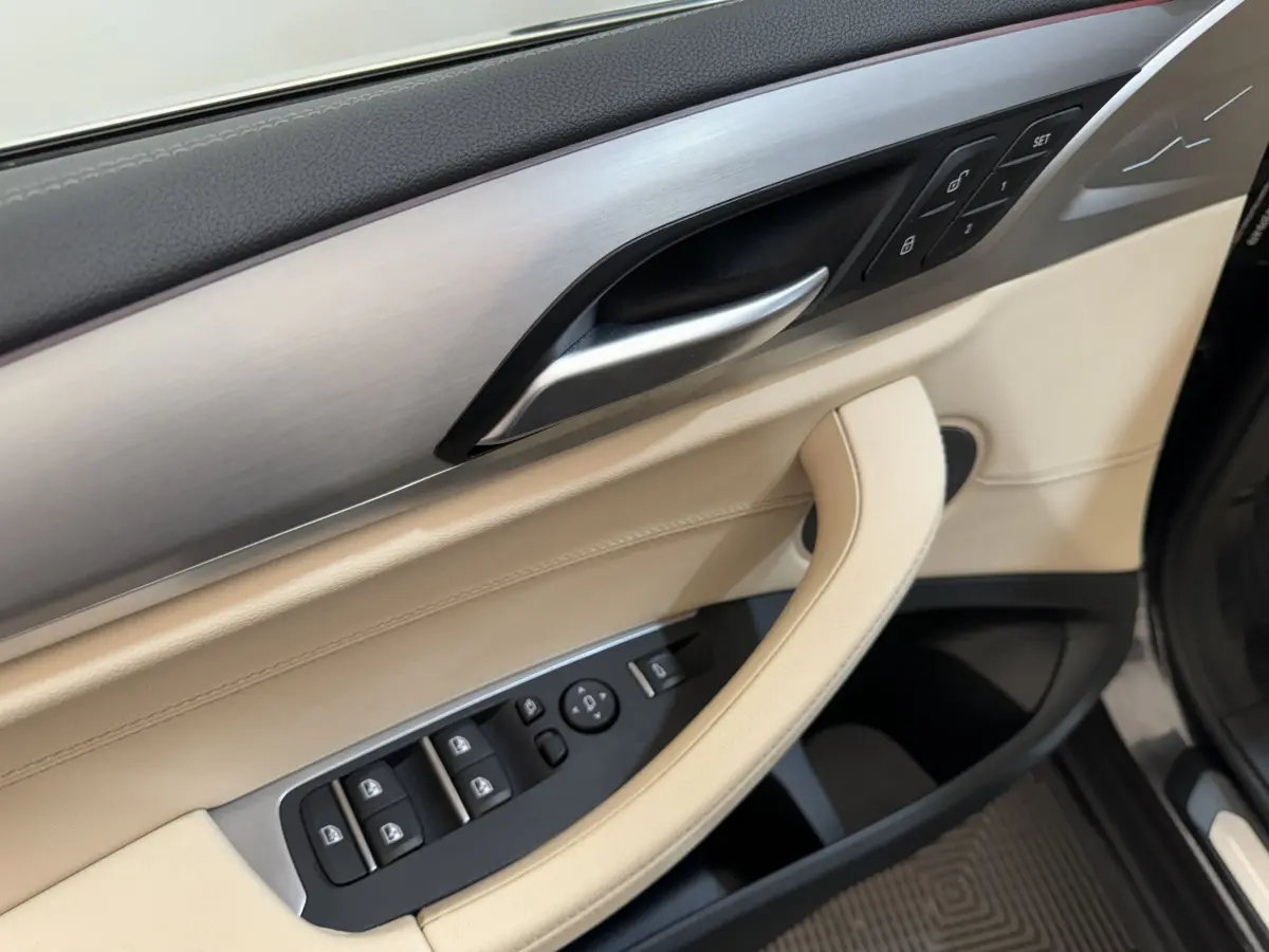 Détail de la porte avant gauche beige et aluminium brossé du BMW X3 xDrive30d 2018 avec commandes de vitres et mémoires de sièges.