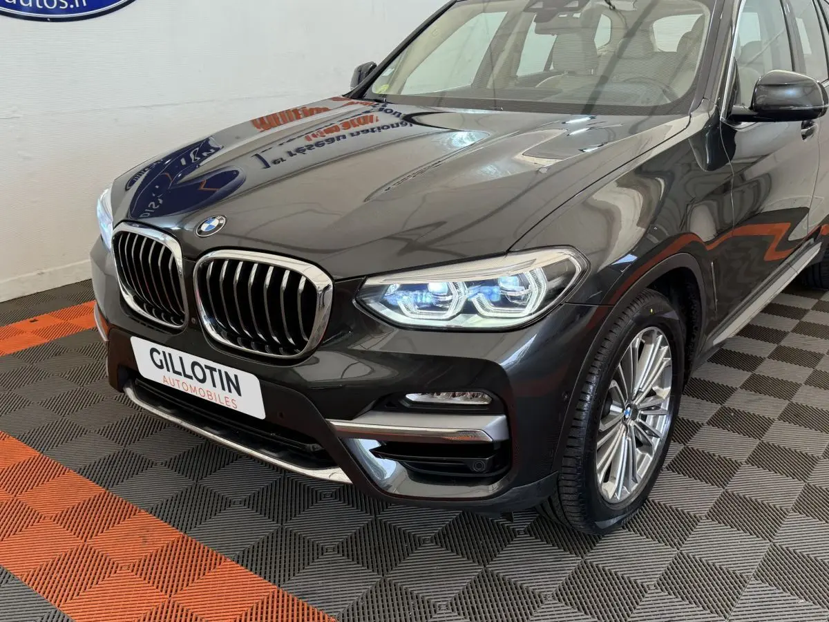 Vue 3/4 avant droit d’un BMW X3 gris foncé avec calandre chromée et phares LED allumés.