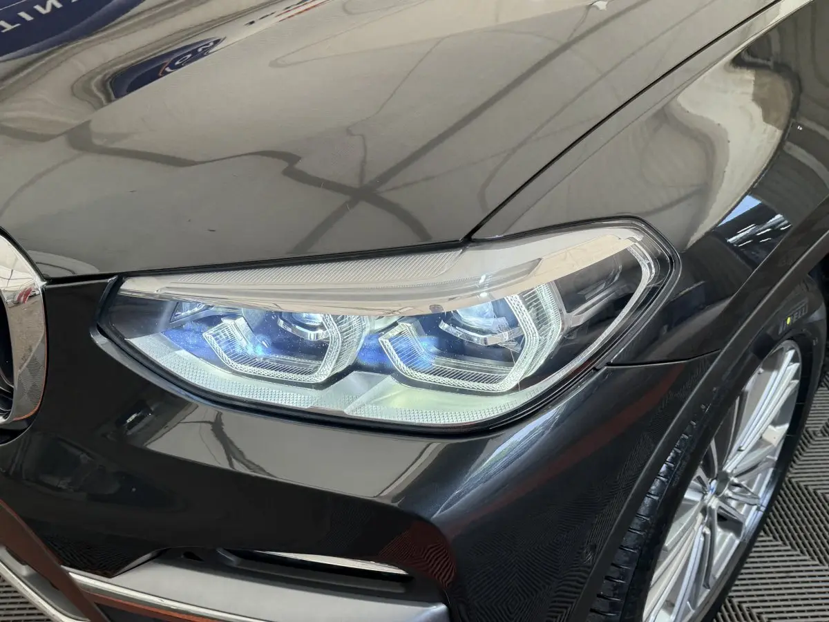Gros plan sur le phare avant droit LED d'un BMW X3 gris foncé, avec jante alliage visible en arrière-plan.