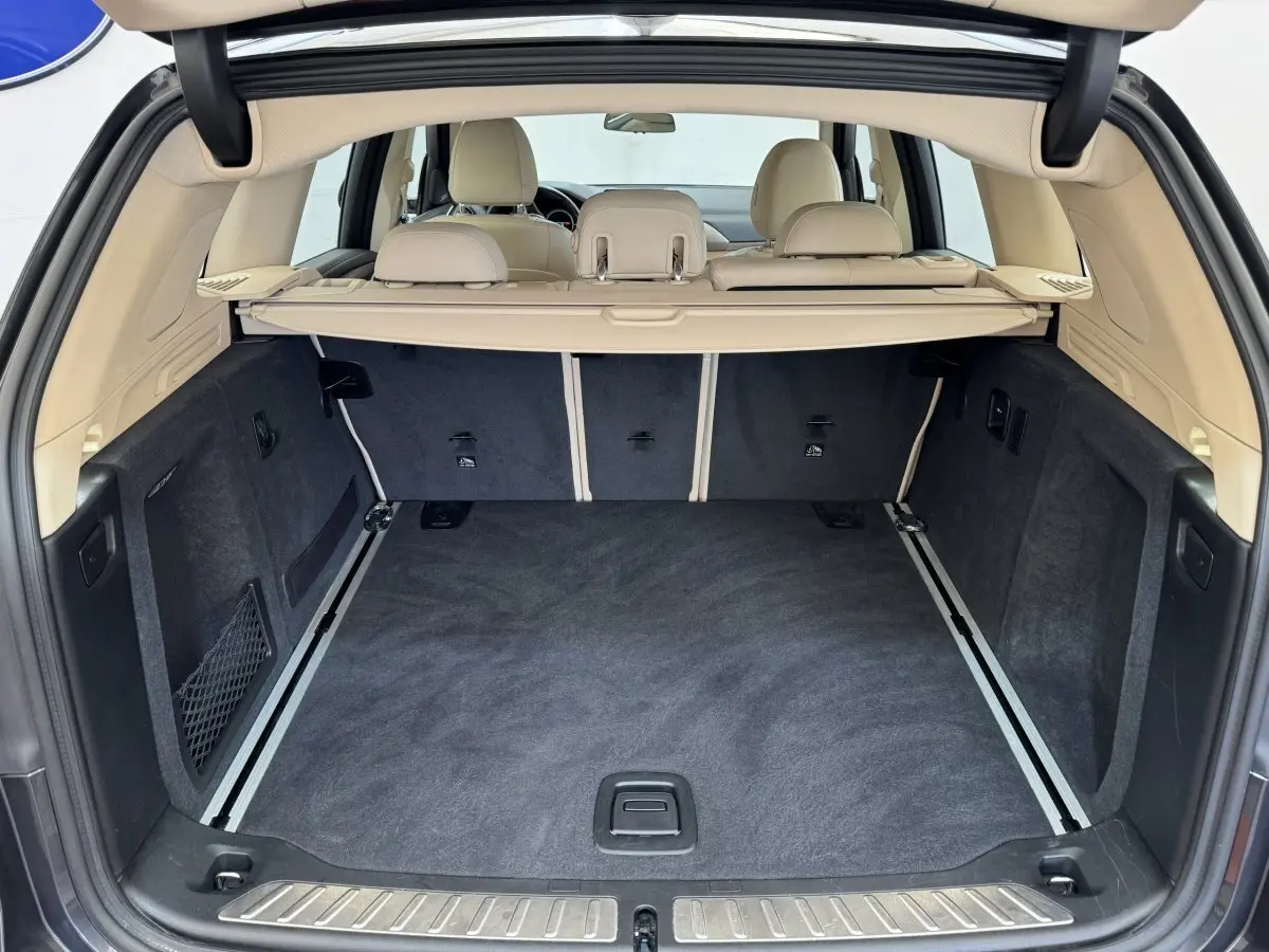 Coffre ouvert d'un BMW X3 gris foncé, vue arrière montrant l'intérieur beige et le tapis noir du coffre spacieux.
