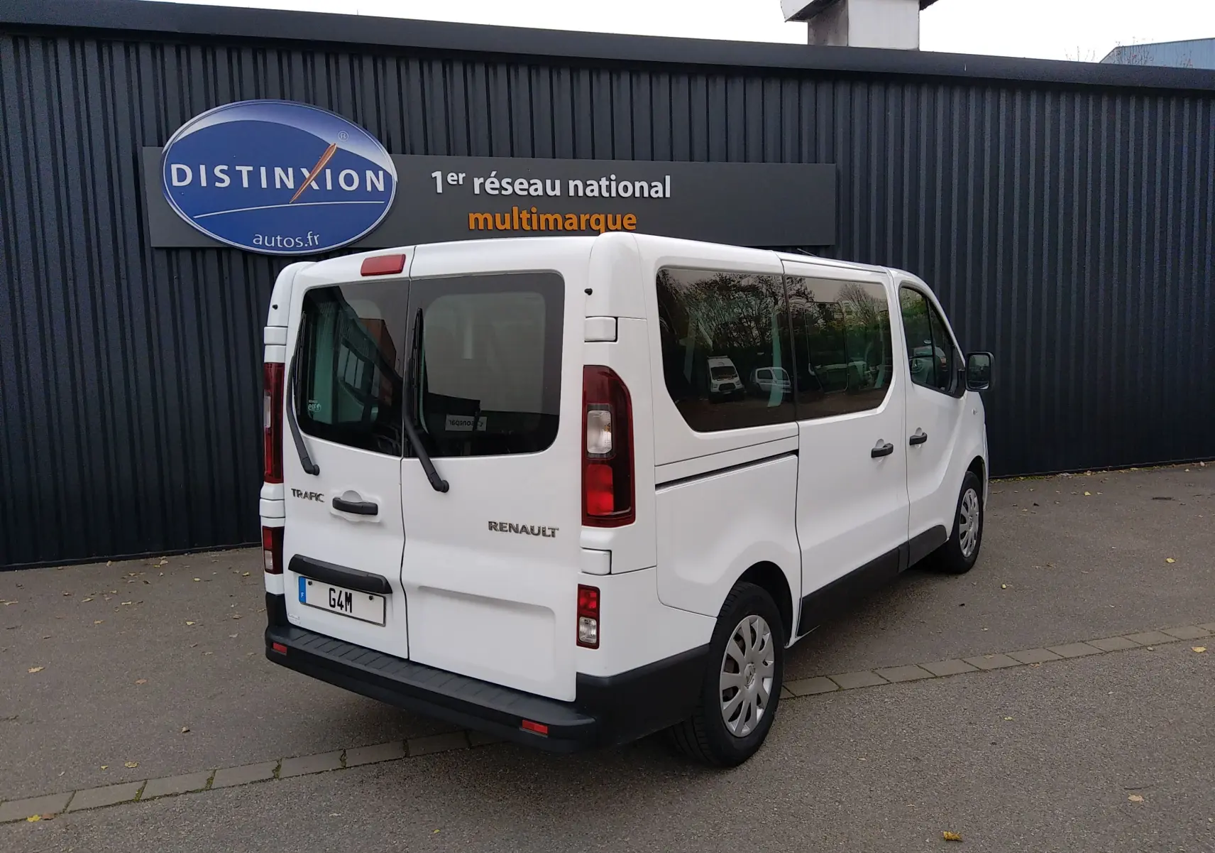 Renault Trafic Microbus blanc vu en 3/4 arrière droit, avec hayon et vitres teintées sur parking extérieur.