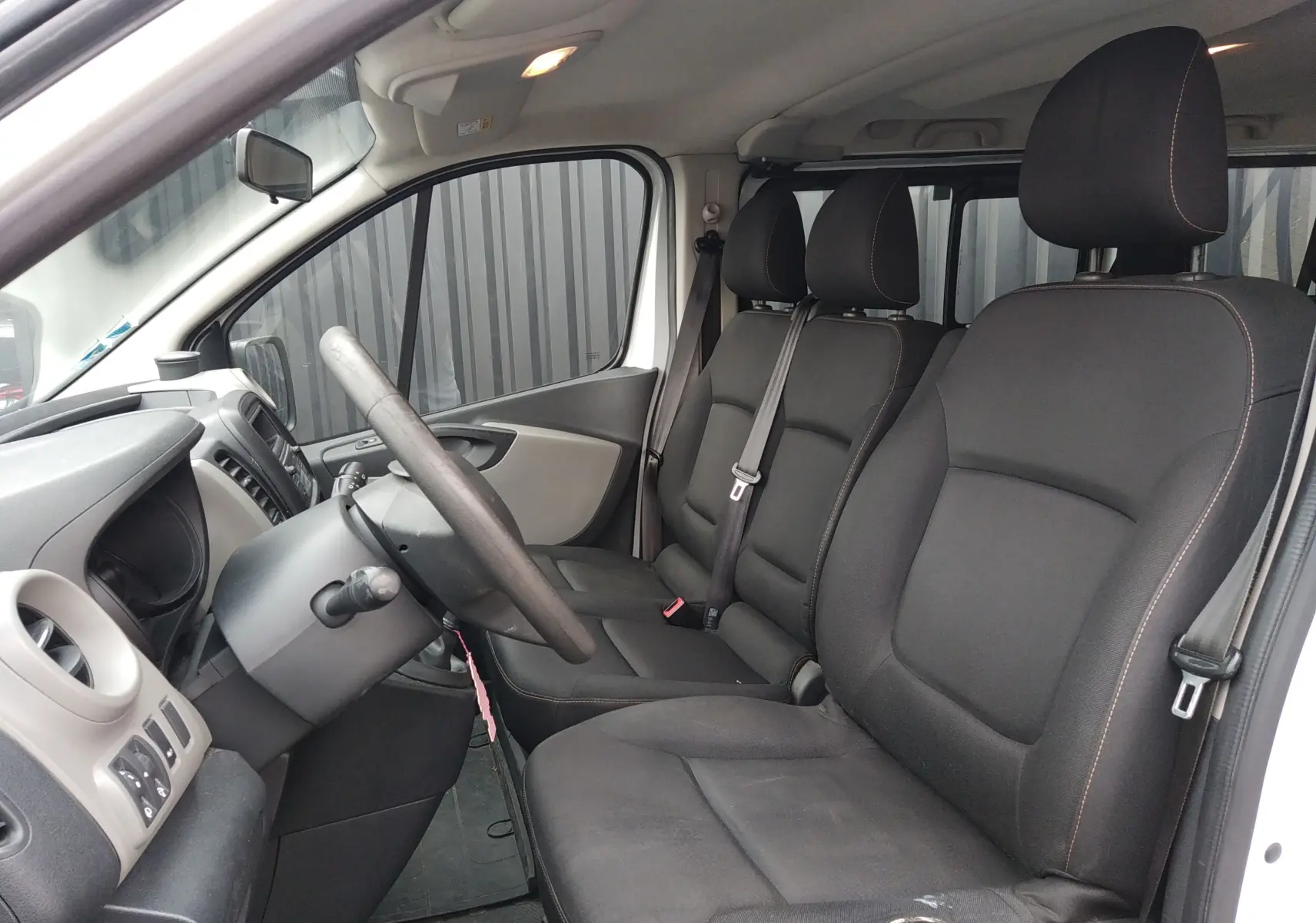 Vue intérieure côté conducteur du Renault Trafic Microbus blanc 2016, sièges tissu noirs avec coutures contrastées.