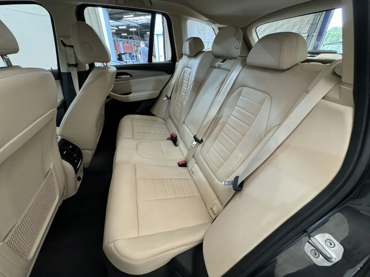 Vue intérieure côté droit des sièges arrière en cuir beige du BMW X3 xDrive30d 2018 avec appuie-têtes et ceintures visibles.