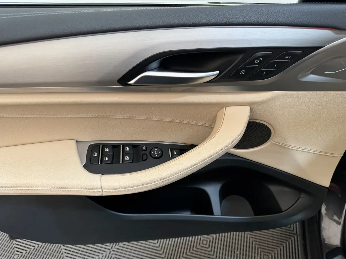Gros plan sur la porte côté conducteur beige et noire de BMW X3 2018 avec commandes de vitres et verrouillage.