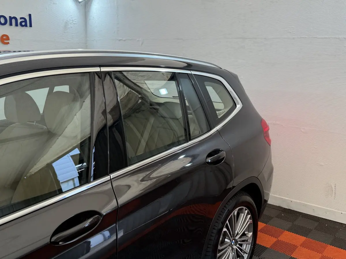 Vue côté arrière droit d'un BMW X3 gris foncé avec jantes alliage et intérieur clair visible à travers les vitres.