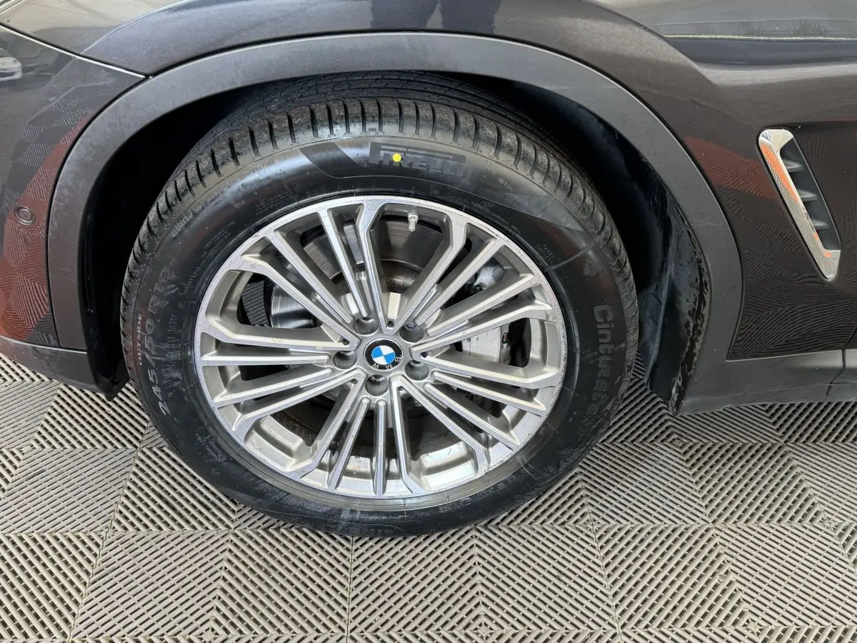 Gros plan sur la roue avant gauche d'un BMW X3 gris foncé avec jante alliage multi-branches et logo BMW central.