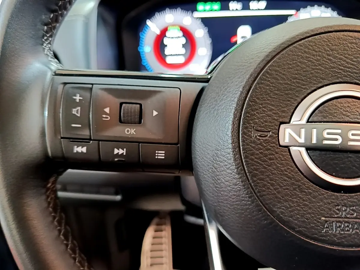 Gros plan sur le volant en cuir noir du Nissan Qashqai e-Power 2023 avec commandes multifonctions et tableau de bord numérique.