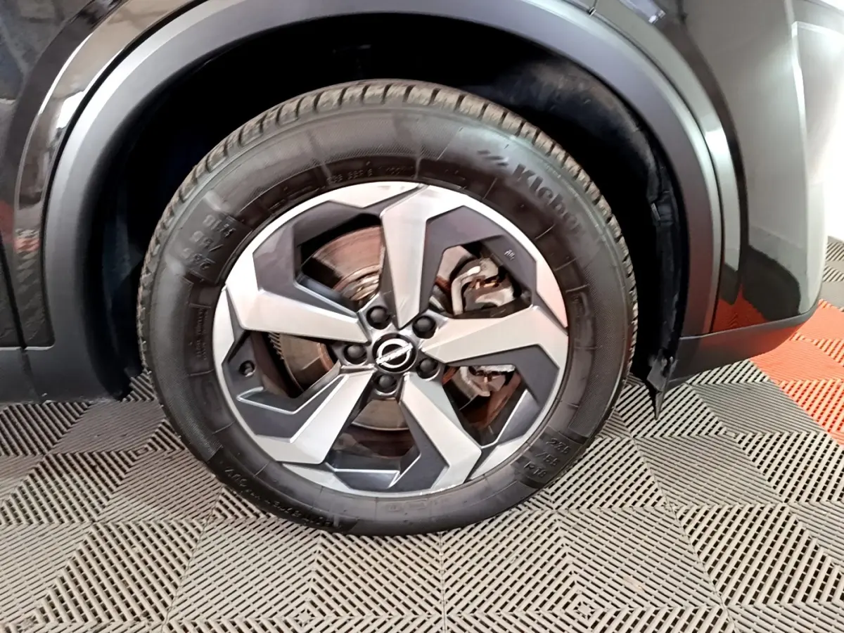 Gros plan sur la roue avant droite du Nissan Qashqai noir, mettant en valeur la jante alu bicolore au design moderne.