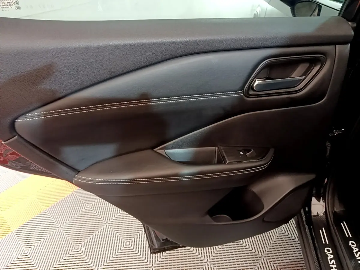Vue intérieure côté gauche de la porte avant noire du Nissan Qashqai e-Power avec surpiqûres blanches et poignée alu.
