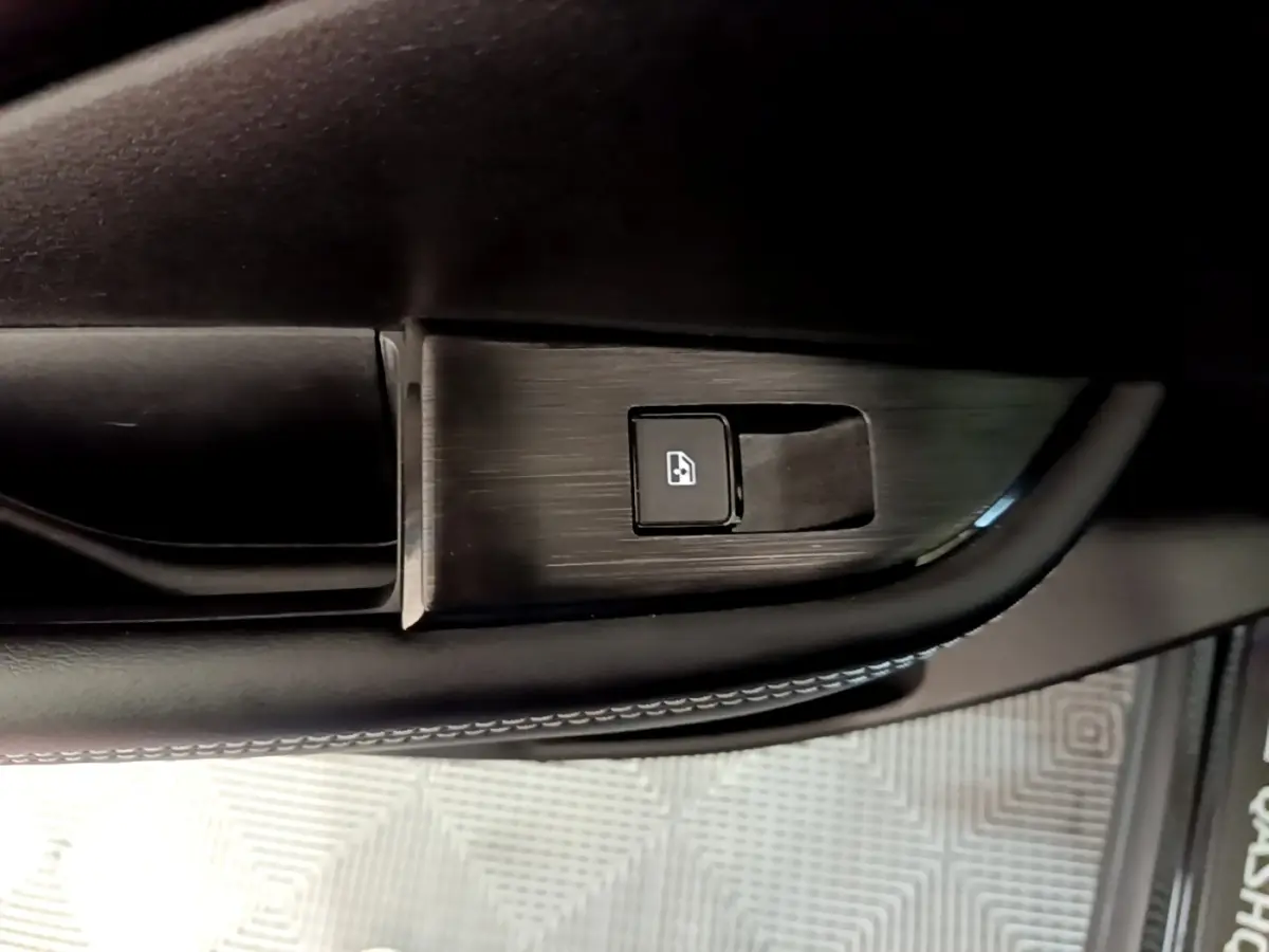 Gros plan sur le bouton de commande de lève-vitre côté conducteur du Nissan Qashqai e-Power noir, intérieur cuir et finition aluminium.