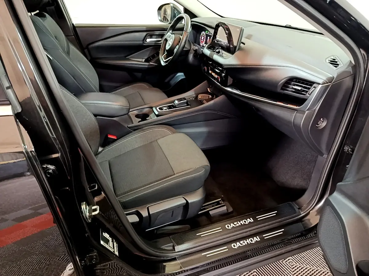 Intérieur avant droit du Nissan Qashqai e-Power noir 2023, volant cuir alu et écran tactile 12,3 pouces visible.