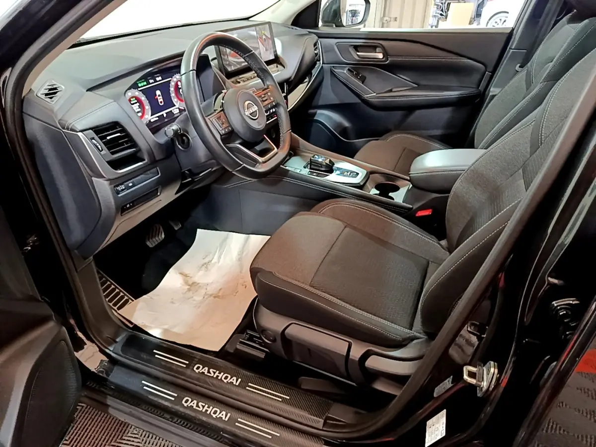 Intérieur avant droit du Nissan Qashqai noir 2023, volant cuir alu, tableau de bord digital et sièges tissu gris.