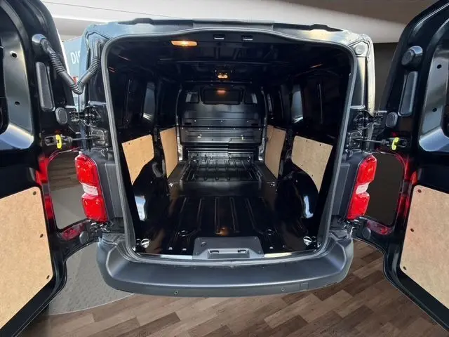 Vue arrière ouverte du Citroën Jumpy noir montrant l’espace de chargement avec cloison pleine et portes battantes ouvertes.