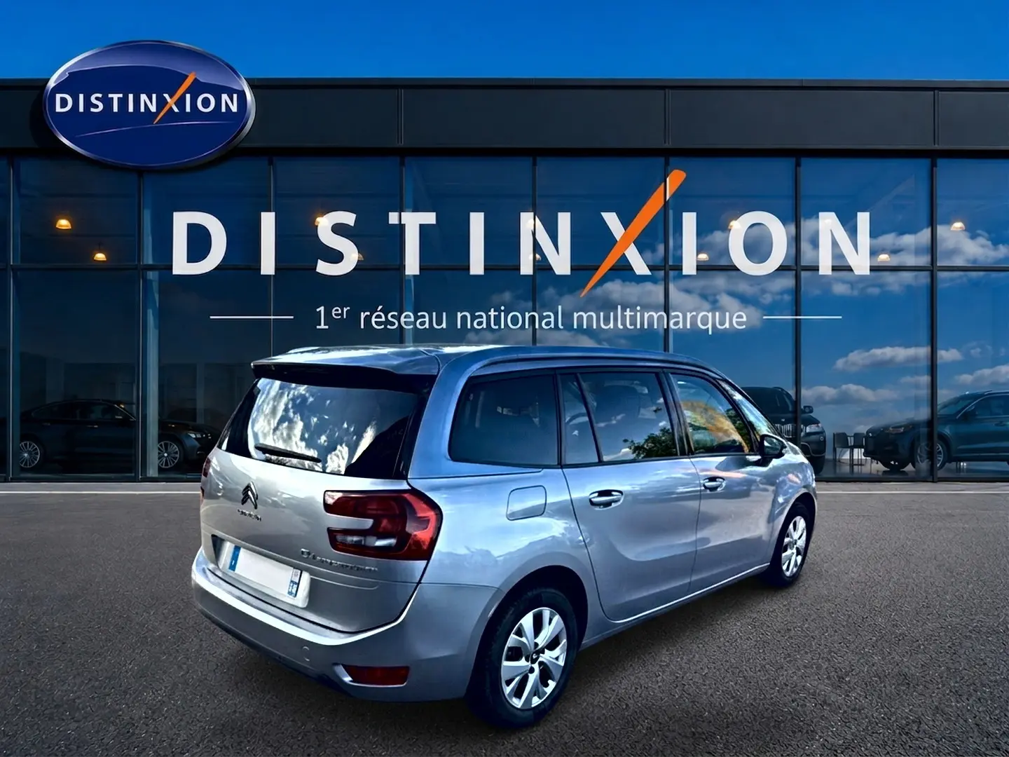 Vue 3/4 arrière droite d'un Citroën Grand C4 Spacetourer gris alu garé devant une vitrine Distinxion.