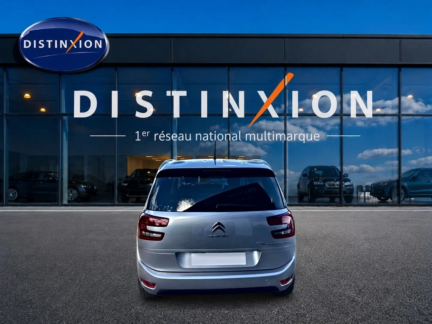 Vue arrière d'un Citroën Grand C4 Spacetourer gris alu garé devant une vitrine avec logo Distinxion.