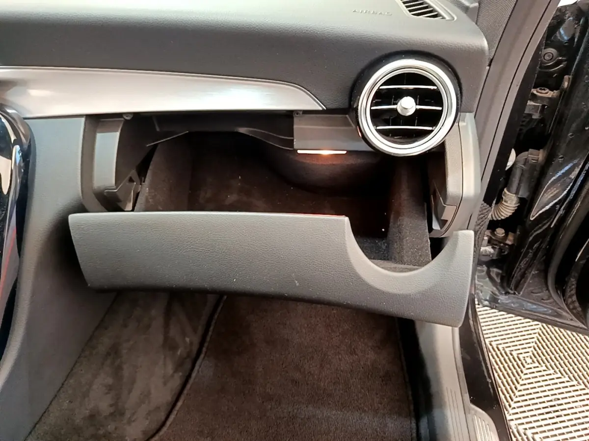Gros plan sur la boîte à gants ouverte côté passager d'une Mercedes Classe C Coupé noire, intérieur sombre et aérateurs ronds visibles.
