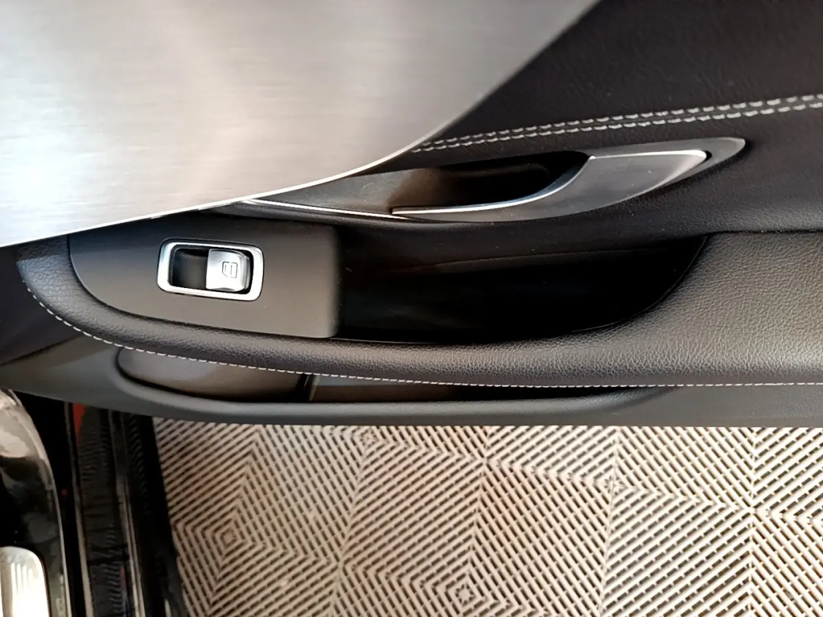 Poignée intérieure côté gauche avec bouton de verrouillage sur porte en cuir noir et insert aluminium d'une Mercedes Classe C Coupé noire.
