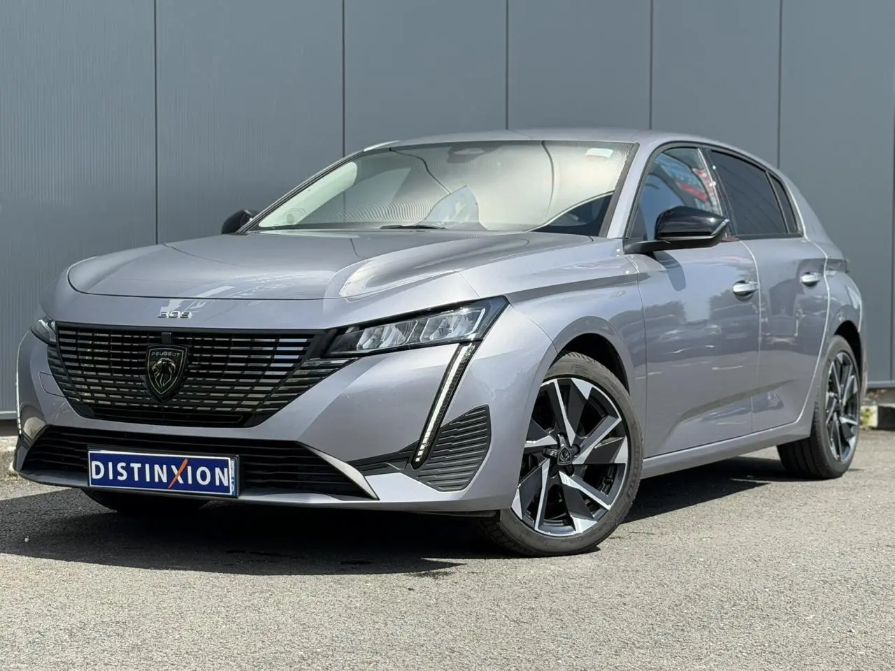 Peugeot 308 gris Artense vue 3/4 avant droit, avec calandre noire et jantes alliage 17 pouces Halong diamantées.
