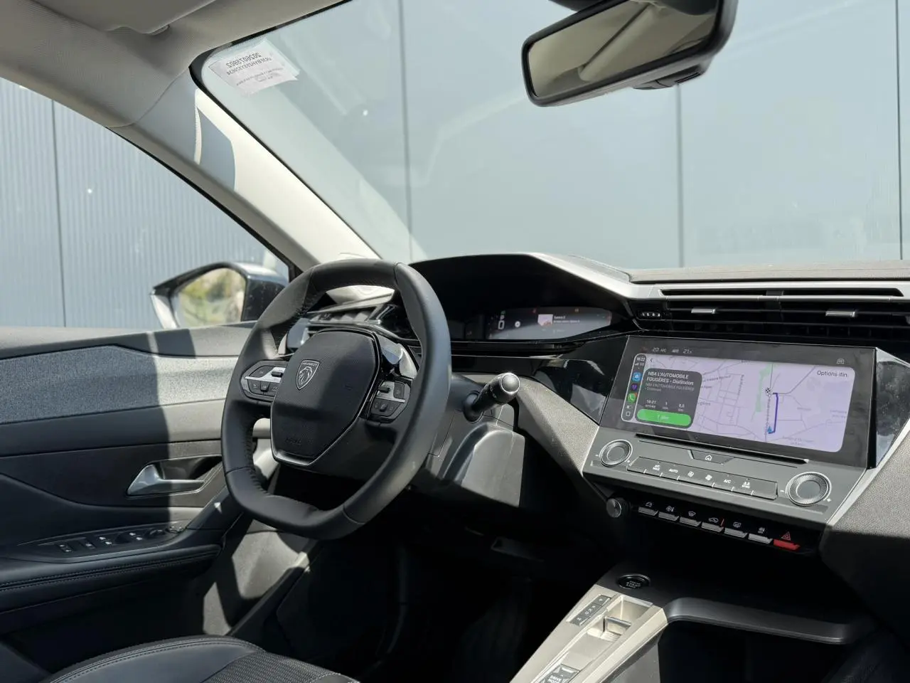 Vue intérieure côté conducteur du Peugeot 308 2025 gris Artense, avec volant cuir et écran tactile central affichant la navigation.
