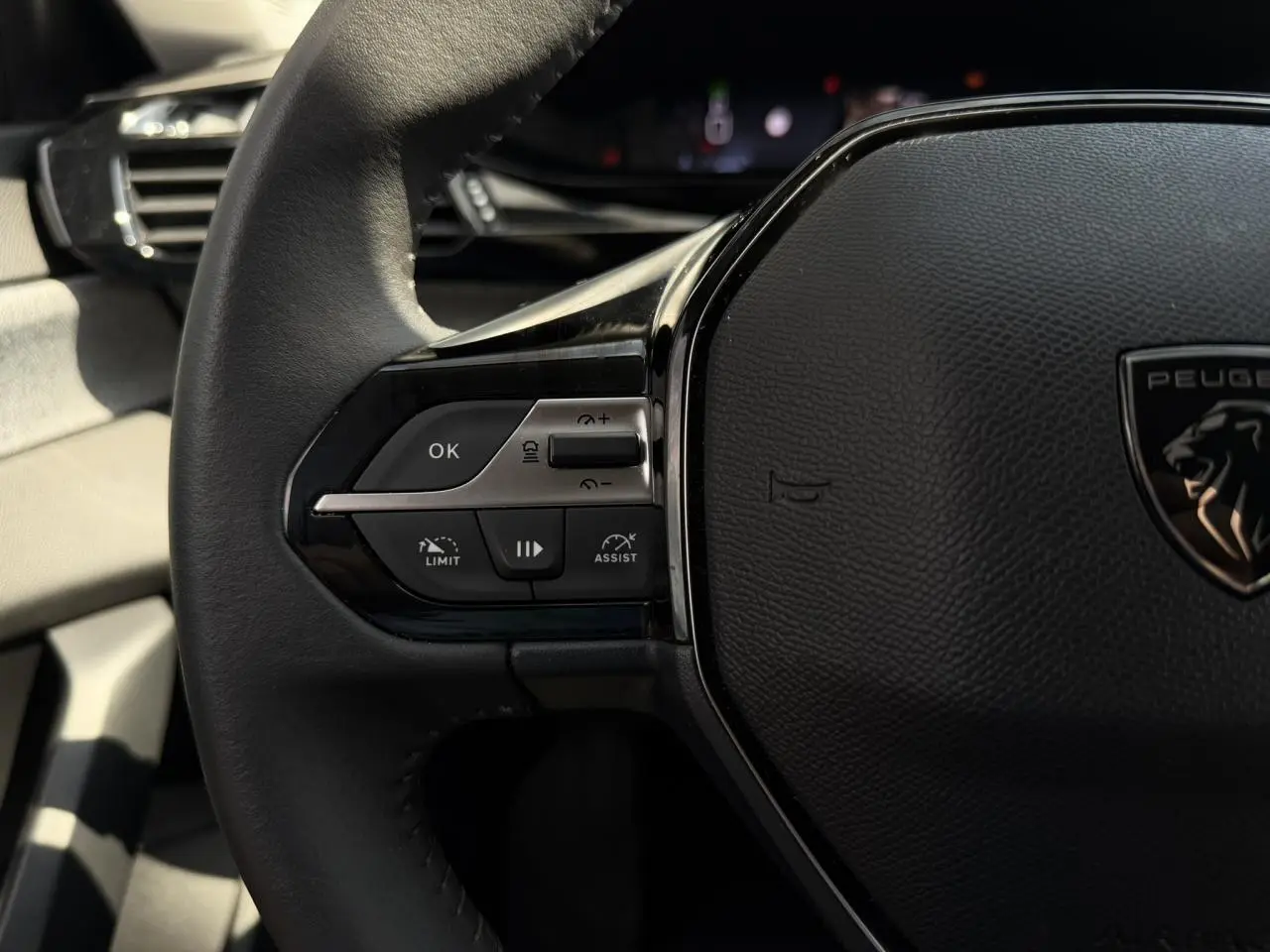 Gros plan sur le volant cuir noir de la Peugeot 308 2025, avec commandes intégrées et logo lion central.