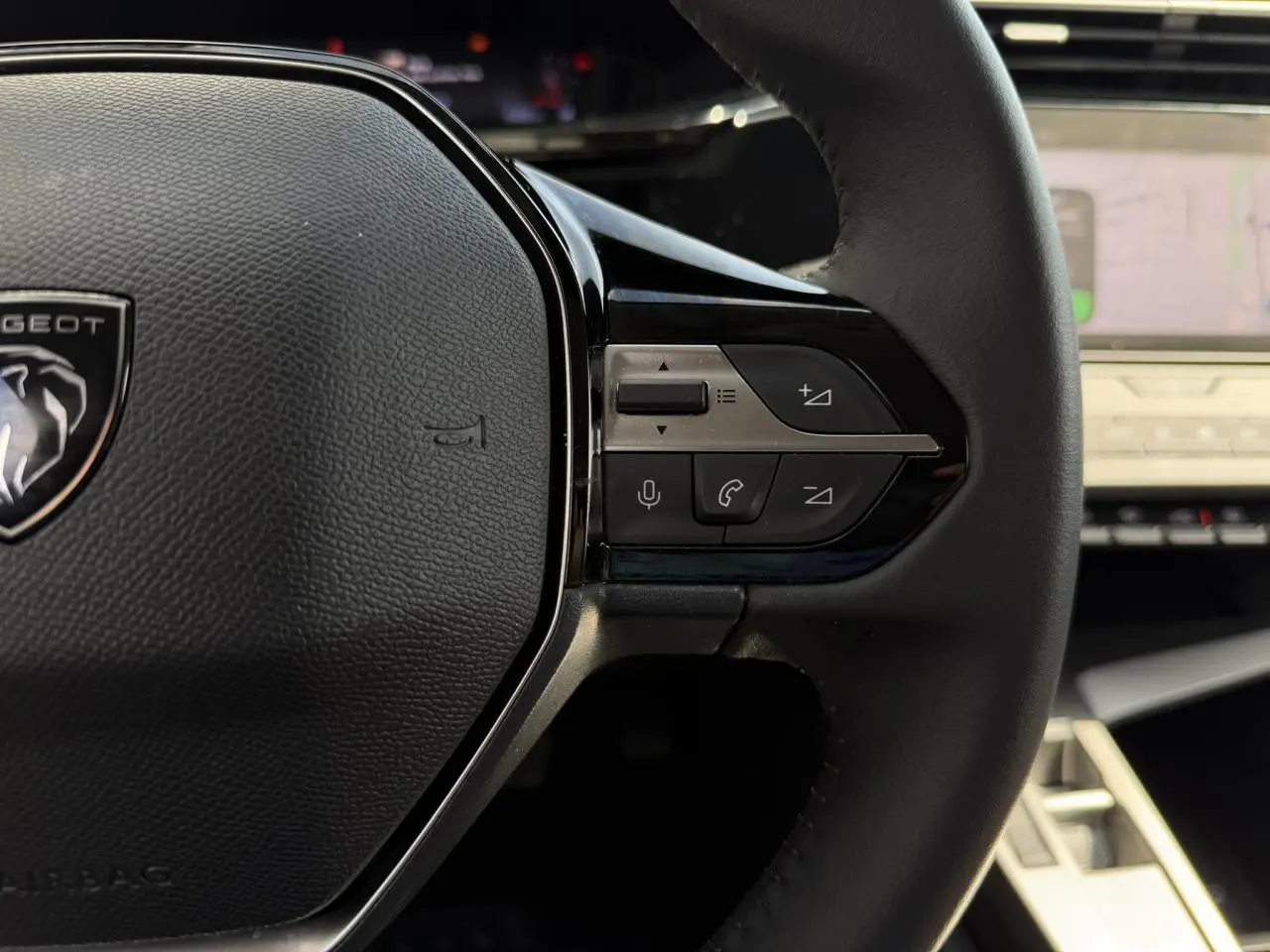 Gros plan sur le volant cuir noir de la Peugeot 308 2025 avec commandes intégrées et écran tactile en arrière-plan.