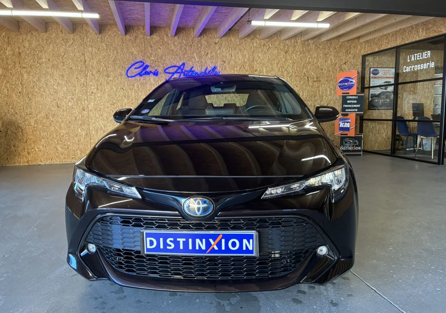 Vue frontale d'une Toyota Corolla 1.8 122 Dynamic noire avec calandre large et phares LED fins dans un showroom.