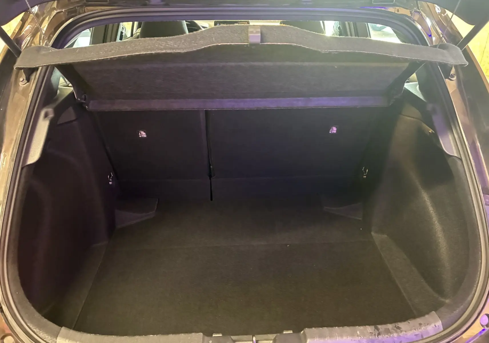 Coffre ouvert vu de l'arrière d'une Toyota Corolla noire, montrant l'espace de chargement et la tablette cache-bagages.