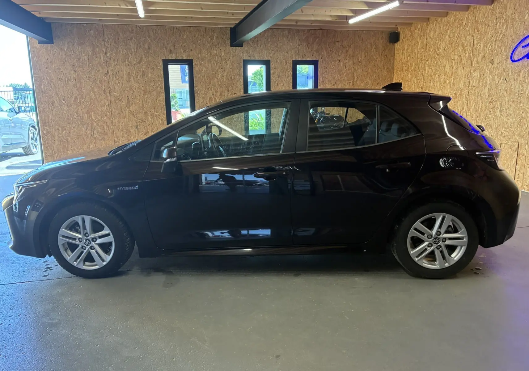 Profil côté gauche de la Toyota Corolla 1.8 122 Dynamic noire, hybride essence, avec jantes alu et rétroviseurs électriques.