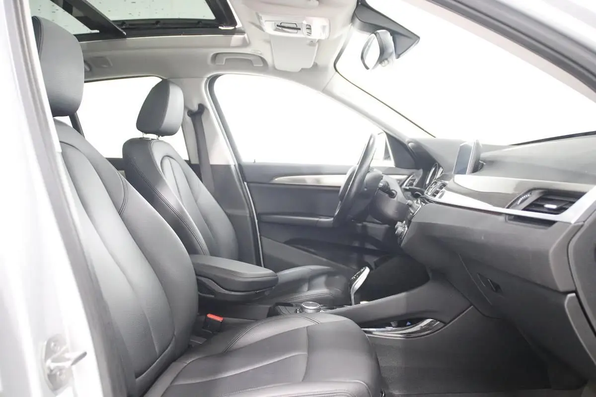 Vue intérieure côté conducteur de la BMW X1 2019, sièges cuir noirs et toit ouvrant panoramique visible.