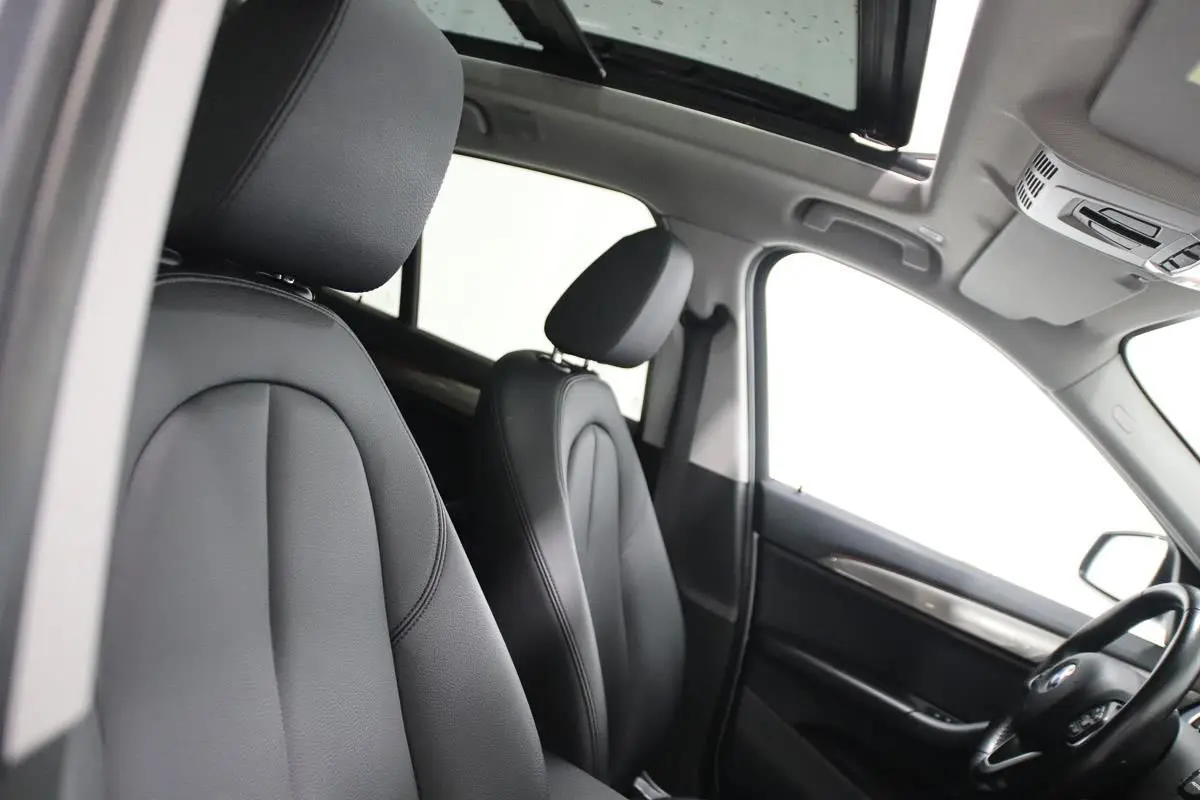 Vue intérieure côté conducteur du BMW X1 argenté 2019, montrant les sièges cuir noirs et le toit ouvrant panoramique.