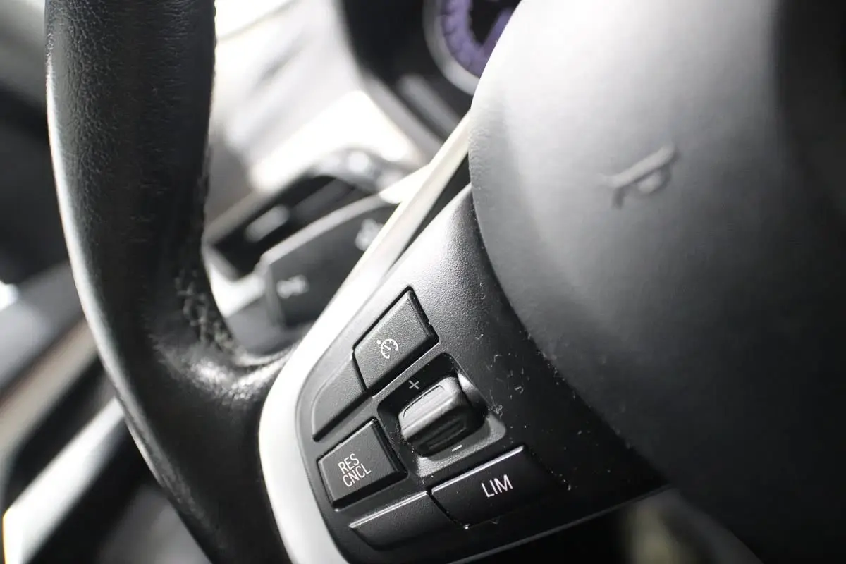 Gros plan sur les commandes de régulateur de vitesse au volant cuir noir du BMW X1 argenté, version sDRIVE 18D BVA X-LINE.