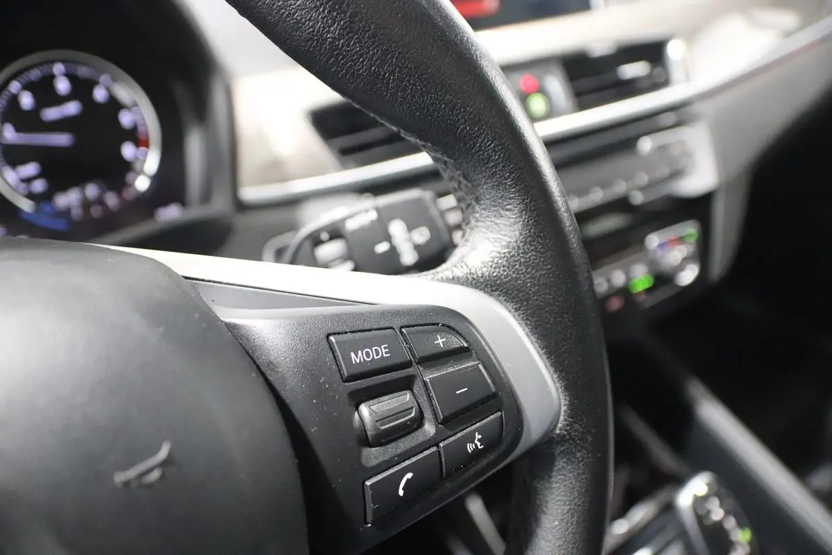 Gros plan sur le volant noir avec commandes multifonctions du BMW X1 sDRIVE 18D 2019, intérieur moderne et lumineux.