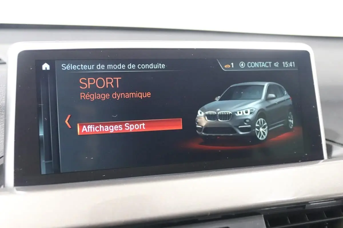 Écran de bord affichant le mode de conduite Sport avec une illustration 3/4 avant d’un BMW X1 argent métallisé.