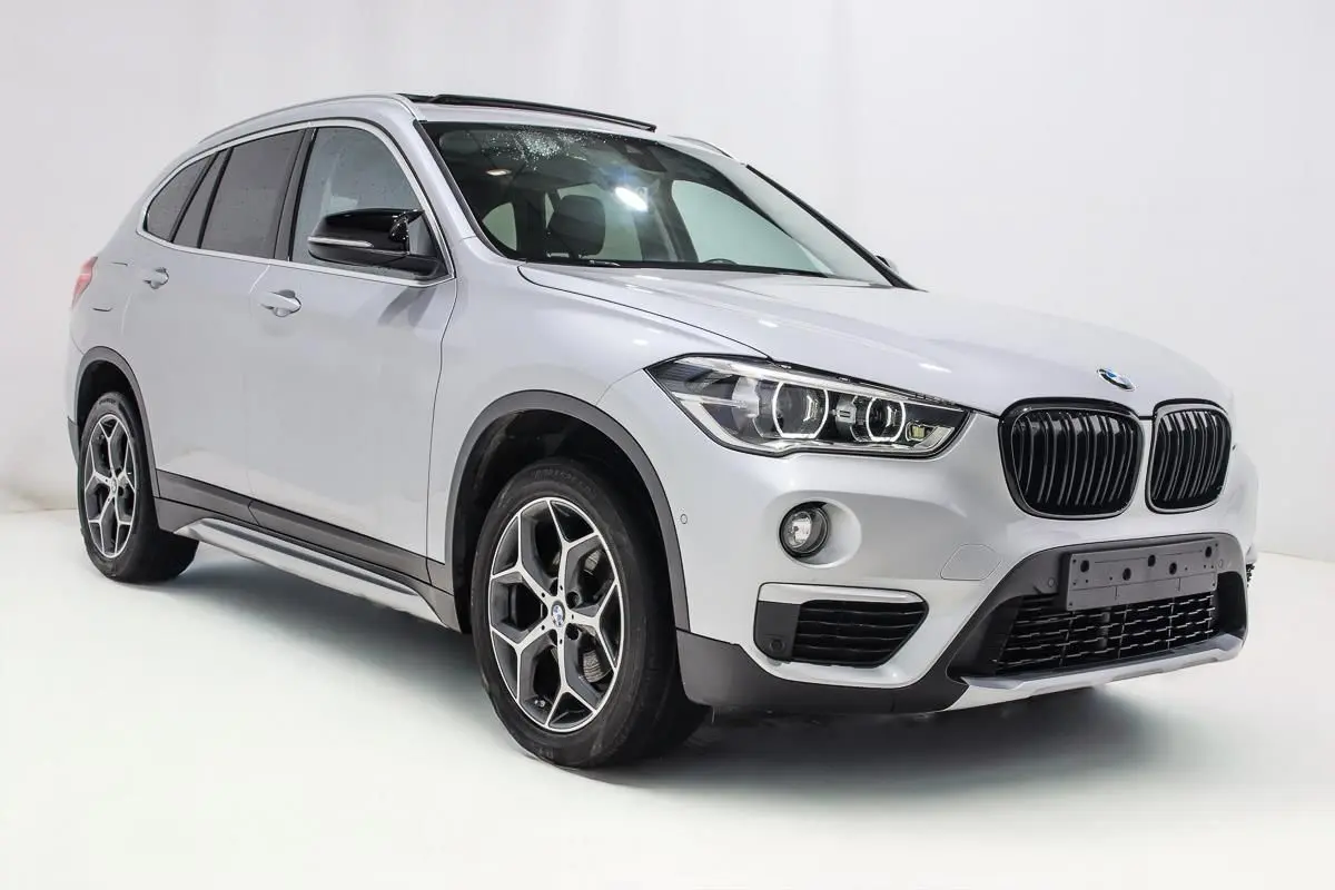 BMW X1 sDrive 18D argent métallisé en 3/4 avant droit, avec toit ouvrant et jantes alliage distinctives.