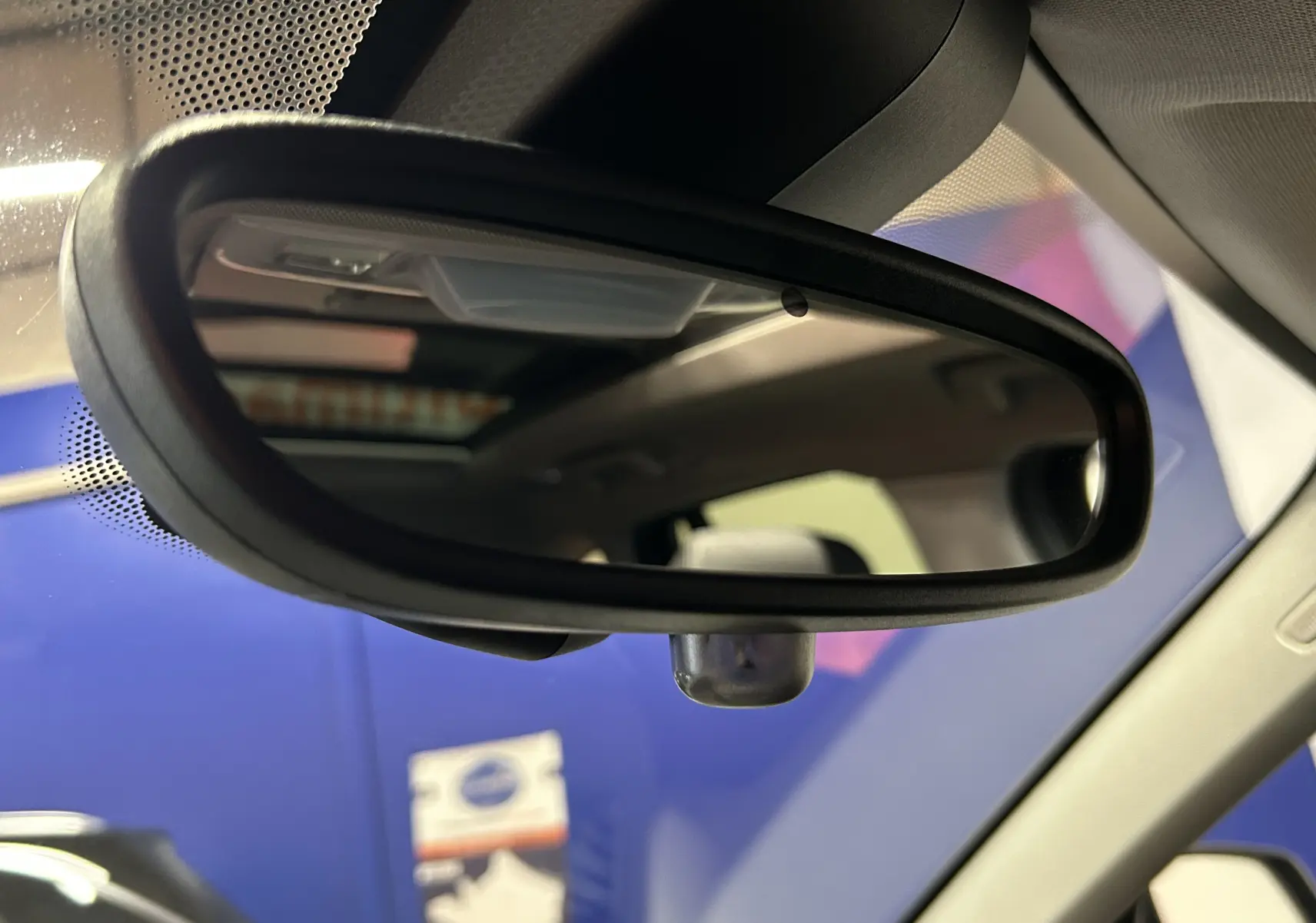 Gros plan sur le rétroviseur intérieur d'une BMW X1 argent métallique, avec toit ouvrant visible en reflet.